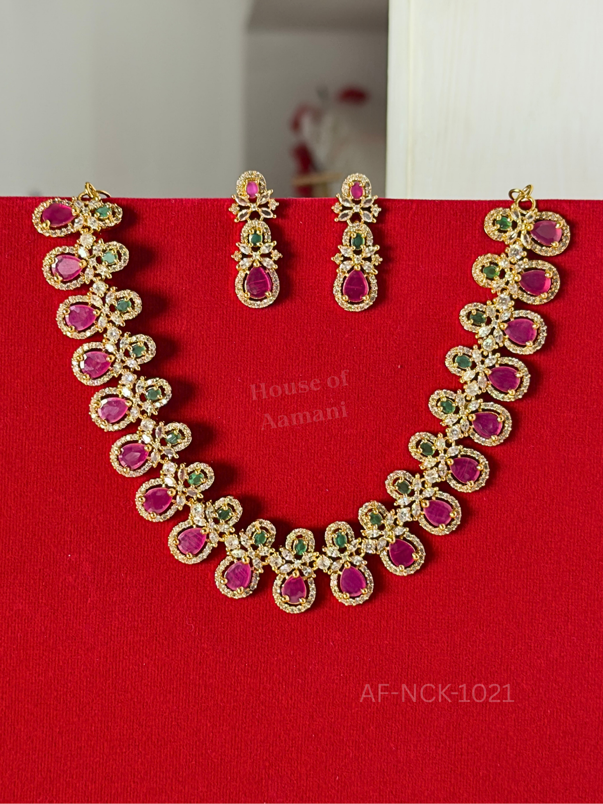 Bold ruby-pink teardrop stones haloed in sparkling white crystals and accented with emerald, paired with elegant matching drop earrings.
