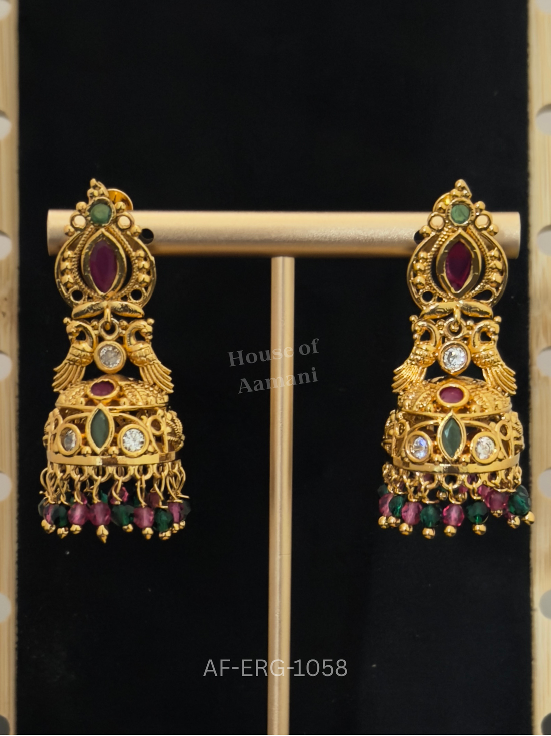 Antique-finish gold jhumkas with twin peacocks, a ruby marquise top, and a ruby-green bead fringe.