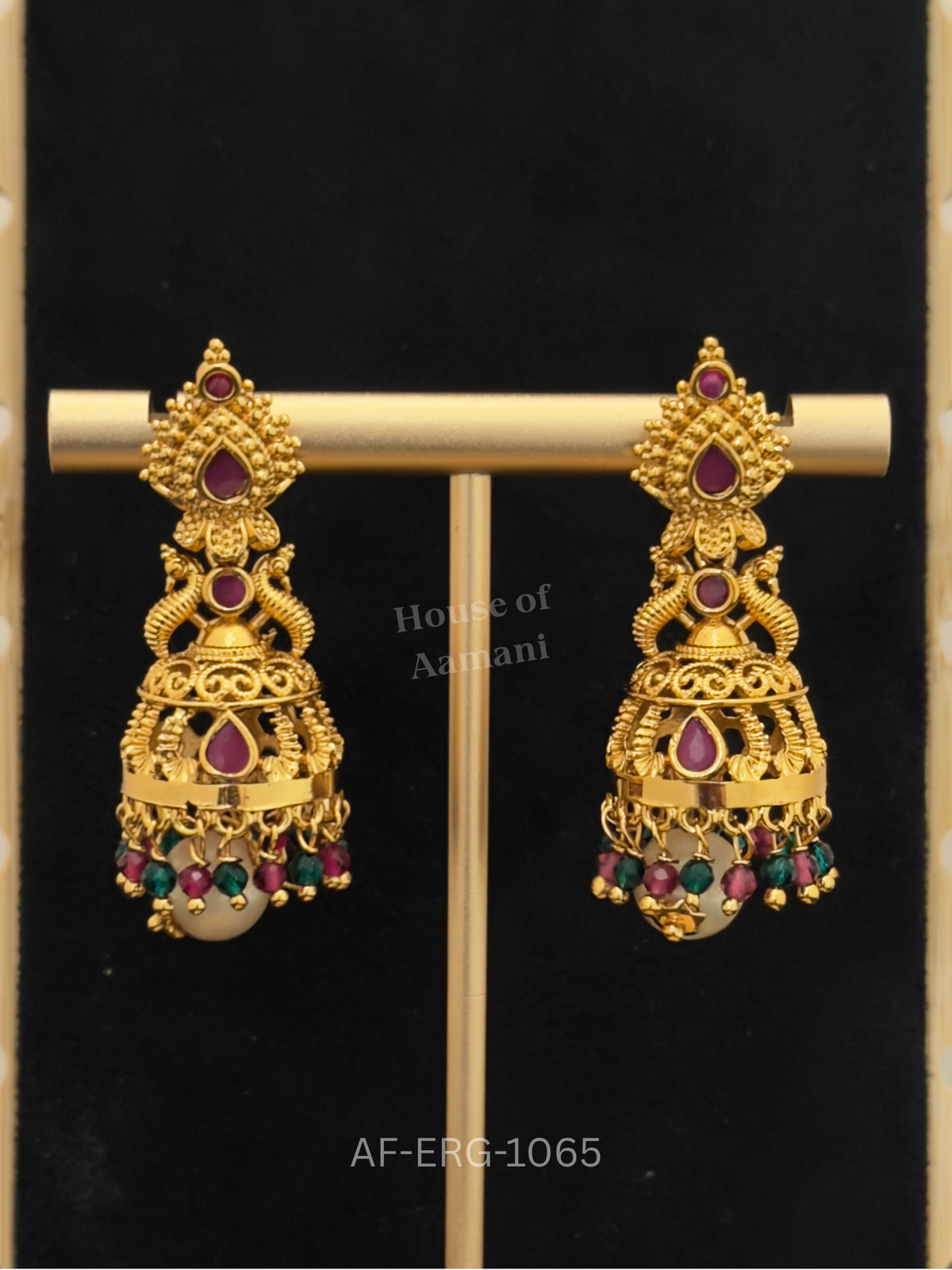 Peacock-inspired antique gold jhumkas set with ruby stones and finished with ruby-green beads and a pearl drop.