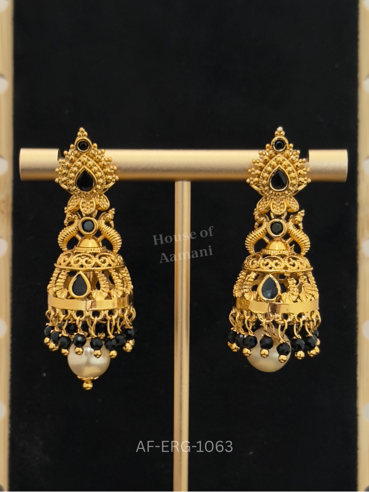 Antique-finish gold jhumkas with twin peacock motifs, black stones, and jet-black bead drops finished with a lustrous pearl.