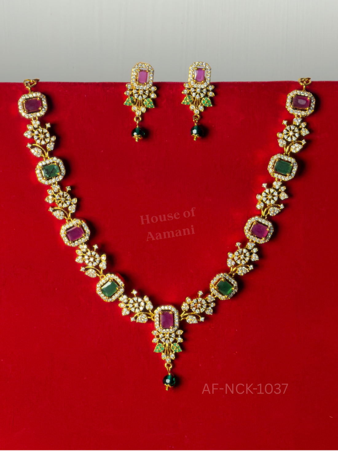 Alternating ruby and emerald stones in crystal halos between floral motifs, finished with an emerald bead drop and matching earrings.