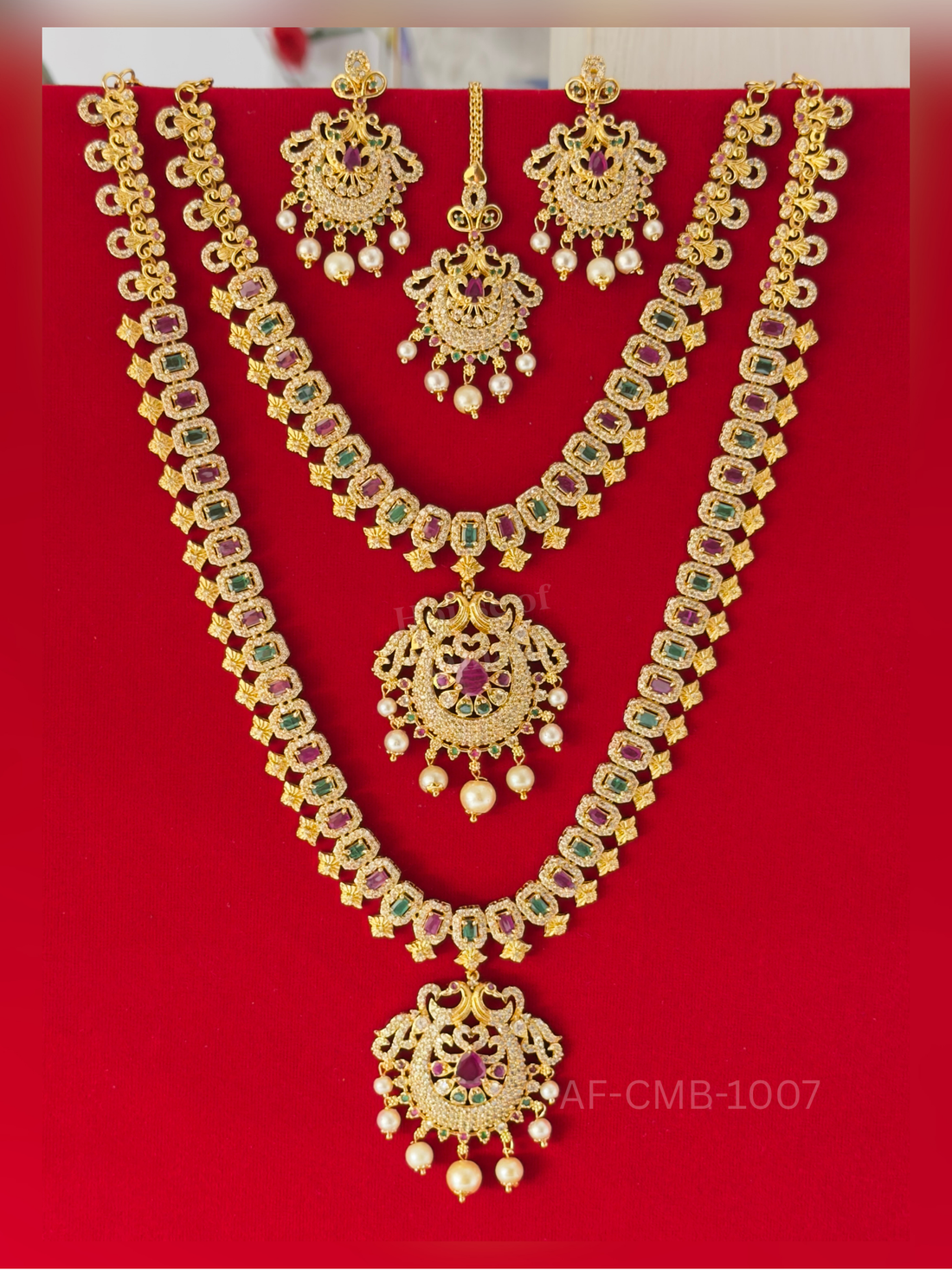 Gold peacock motifs and crystal flowers alternate with ruby and emerald blocks, centred on a Lakshmi temple pendant with pearl drops, plus matching earrings and maang tikka.