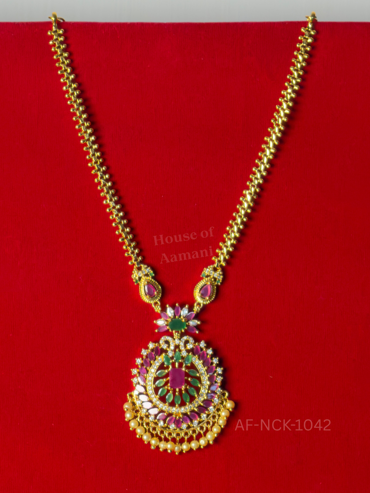 A gold link chain with a round ruby and emerald pendant, fringed with pearl drops.