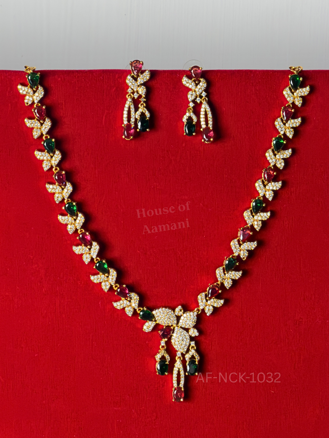 Crystal leaf links alternating with ruby and emerald teardrop stones, ending in a tassel-style pendant with matching earrings.
