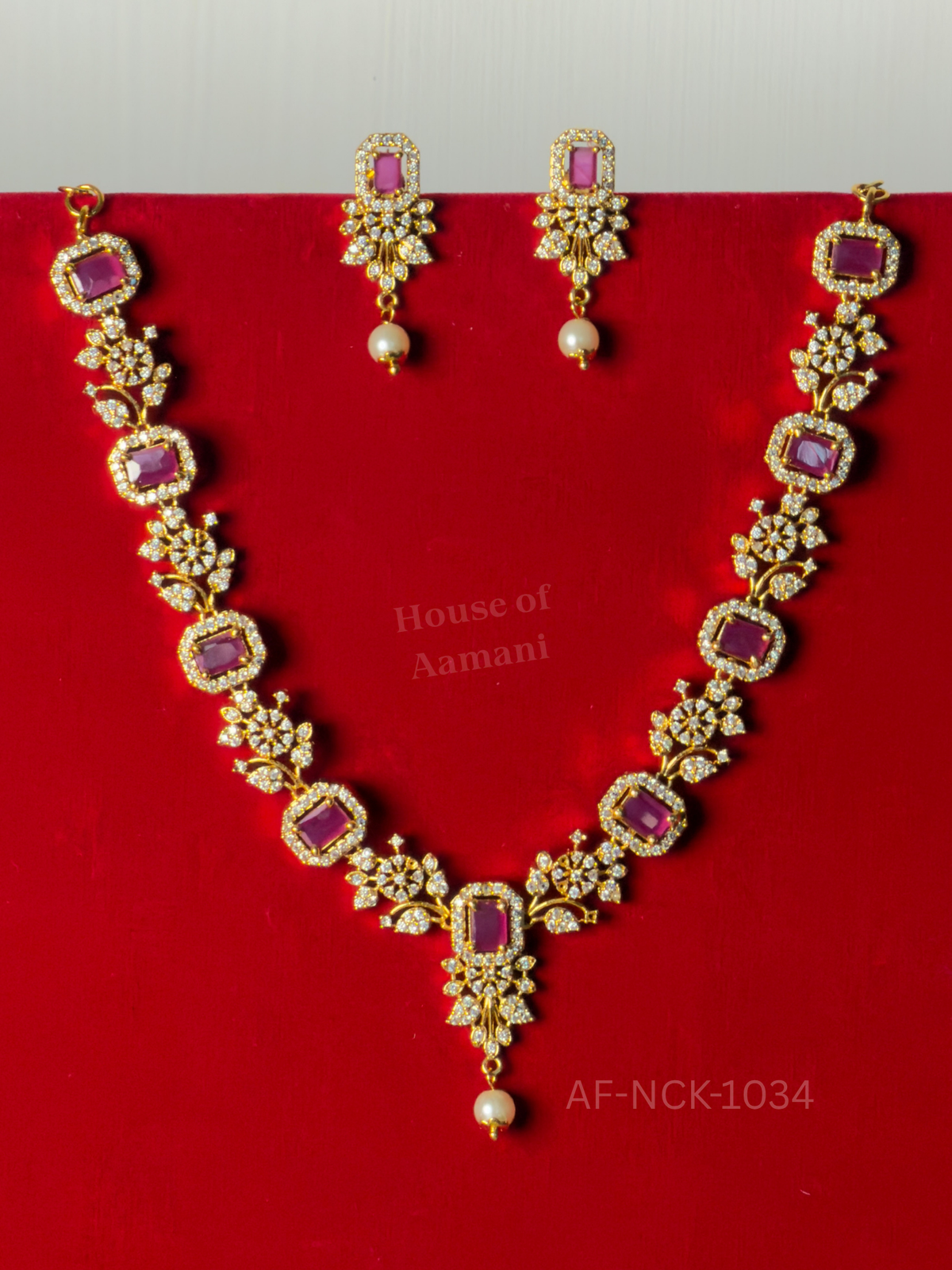 Rectangular ruby stones in crystal halos linked by floral motifs, with a lustrous pearl drop and matching earrings.