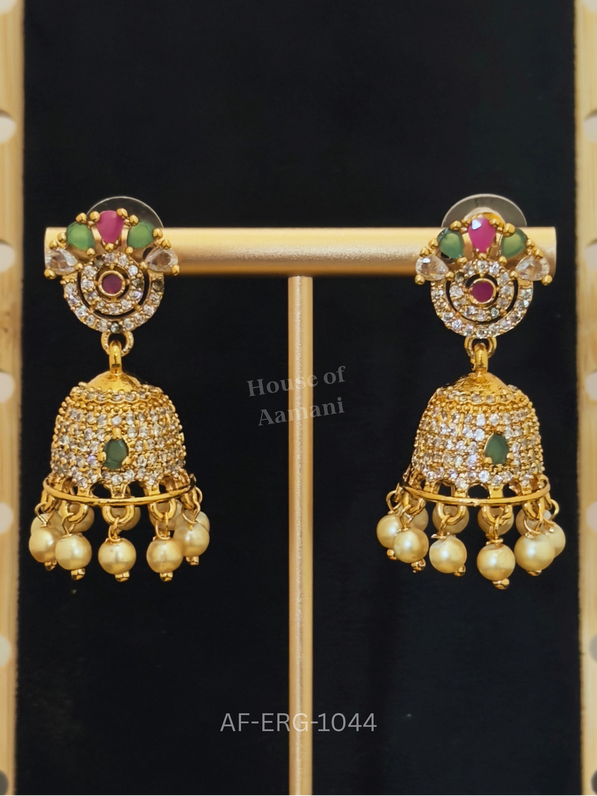 A halo of white crystals with ruby and emerald accents leads to a bell-shaped jhumka fringed with lustrous pearls.