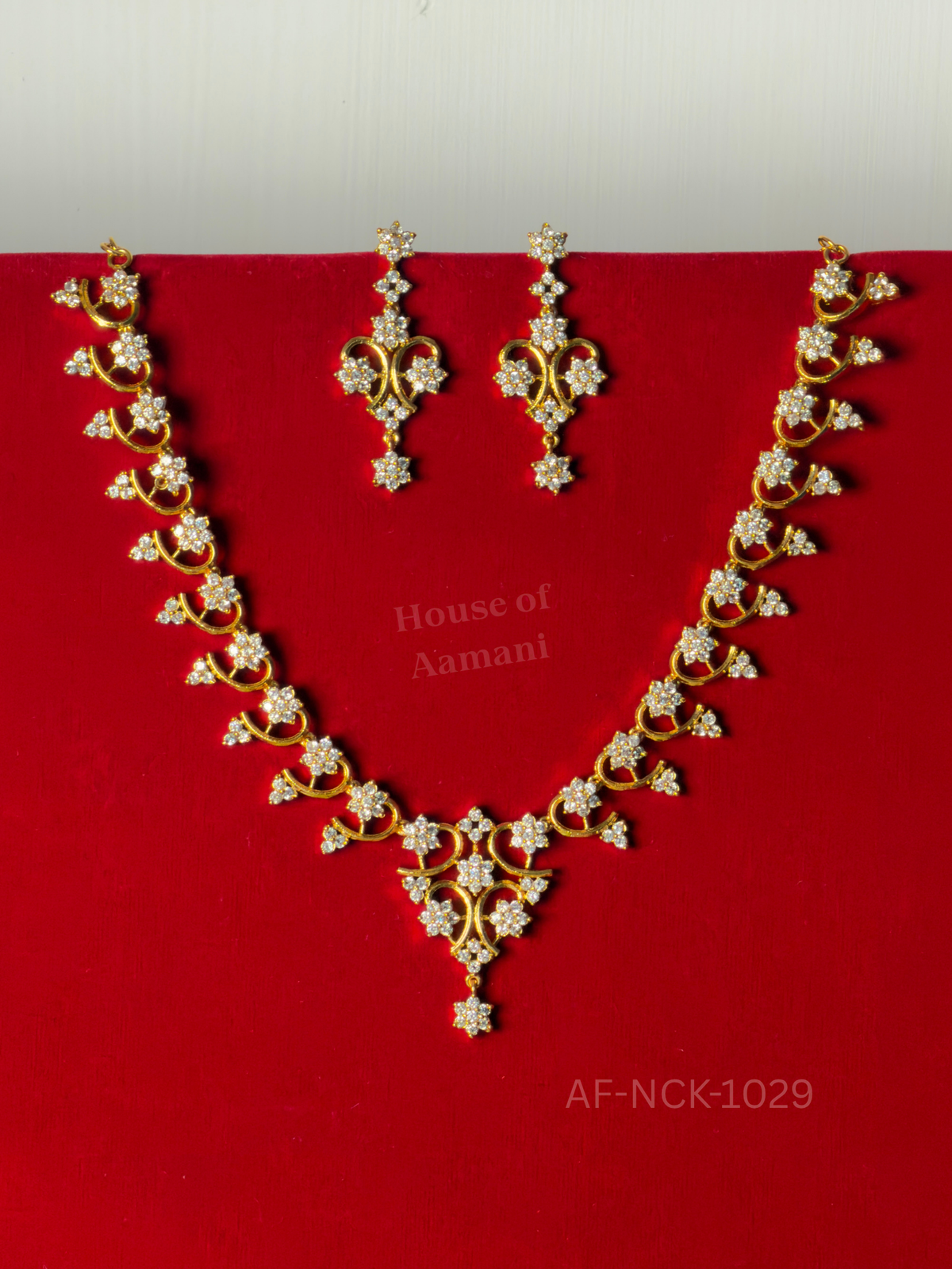 A graceful V-shaped necklace of sparkling white crystal flowers on curling gold vines, with matching drop earrings.