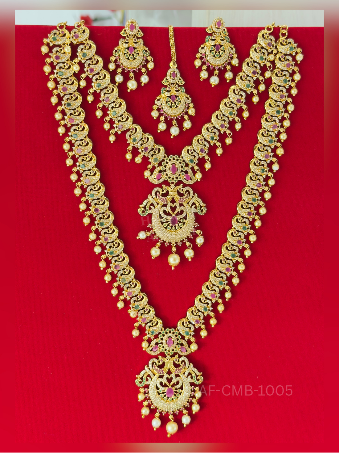 Paisley-shaped peacock links dangling with pearls flow into chandbali pendants, coordinated with matching earrings and a maang tikka.