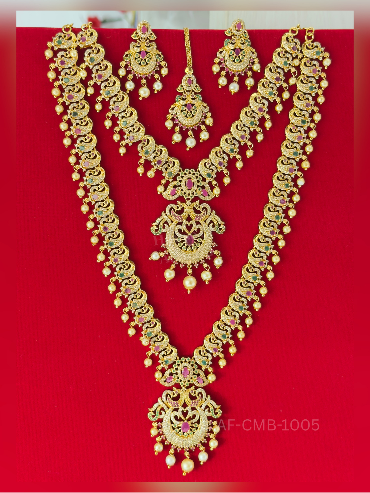Paisley-shaped peacock links dangling with pearls flow into chandbali pendants, coordinated with matching earrings and a maang tikka.