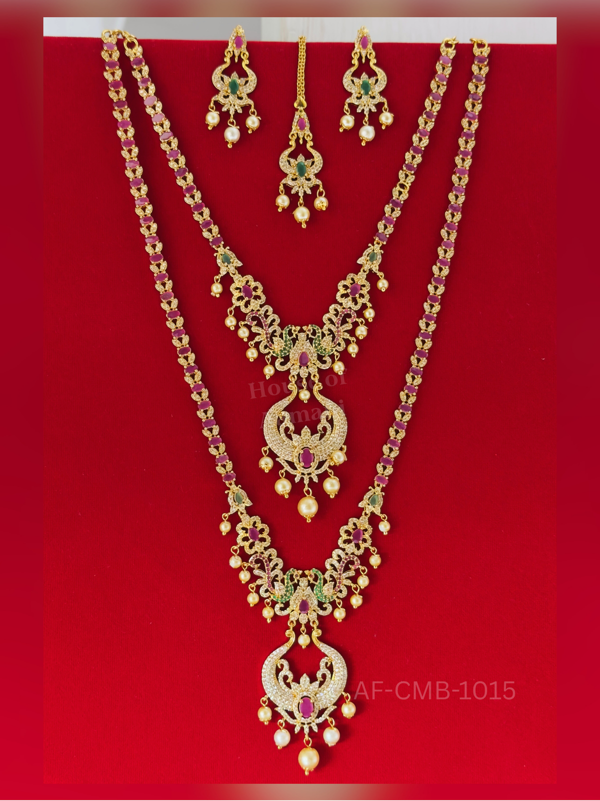 A long chain of oval rubies and crystal leaves ends in a peacock crescent pendant with pearl drops, paired with earrings and maang tikka.