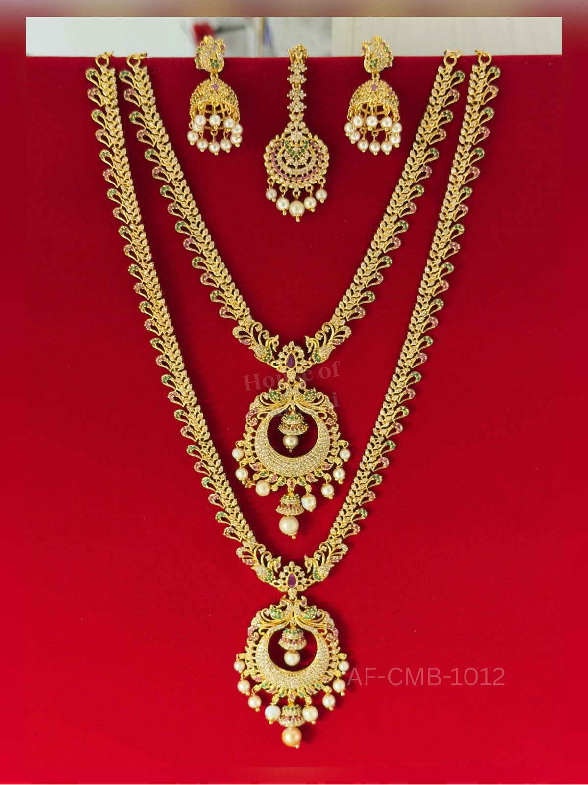 Paisley-shaped links lead to a crescent chaand pendant with peacocks and hanging jhumkas, paired with pearl jhumka earrings and maang tikka.