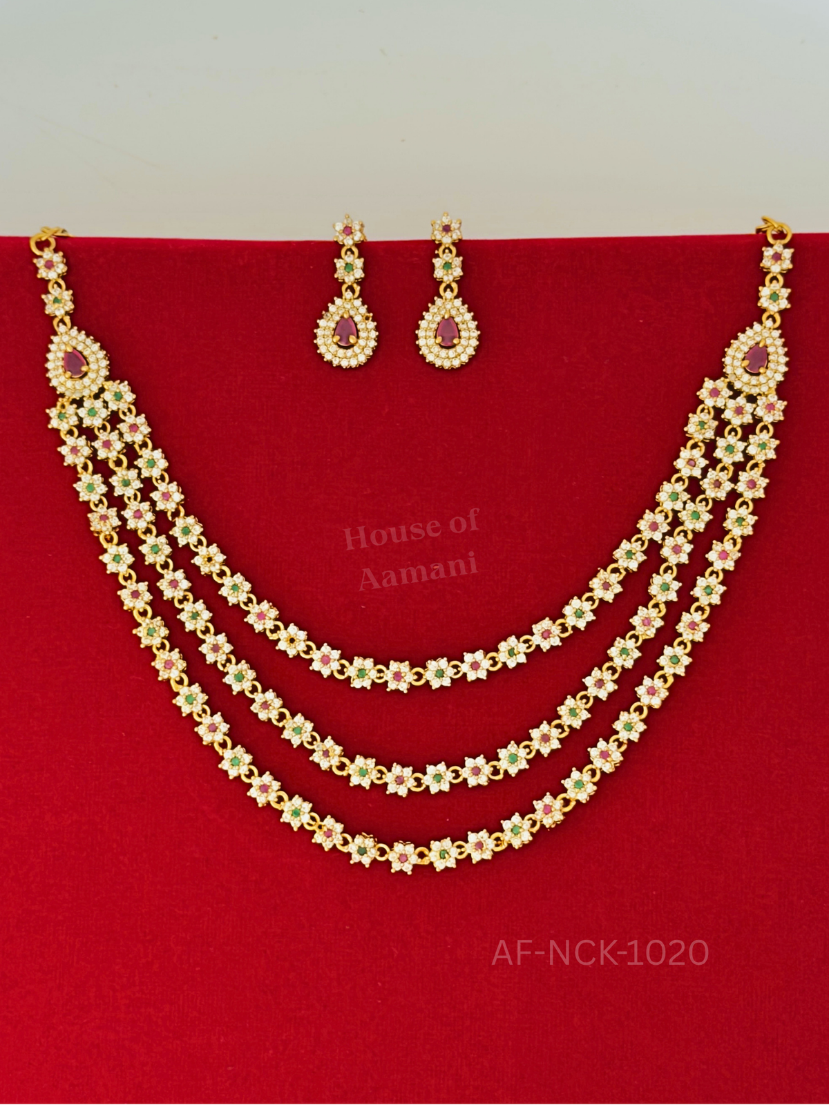 A three-strand gold-plated necklace of sparkling floral links with ruby and emerald accents, finished with teardrop side pendants and matching drop earrings.