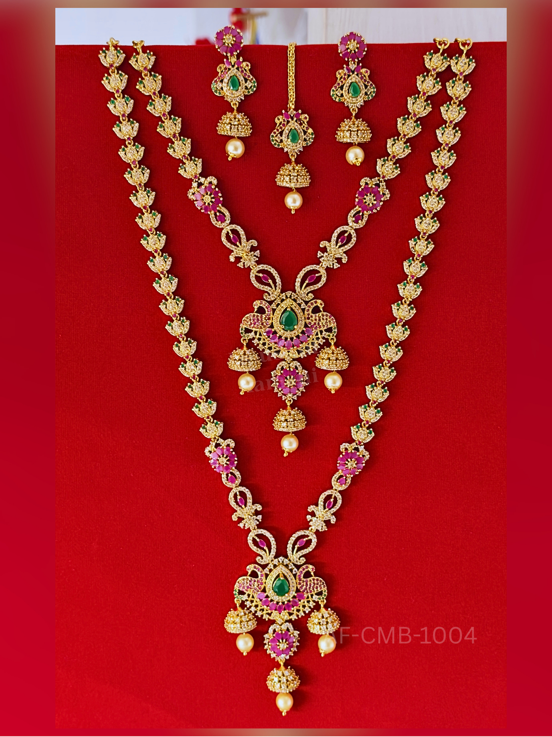Ruby flowers and sparkling butterfly motifs line the long haram and short necklace, finished with ornate teardrop pendants, pearl accents, earrings, and maang tikka.