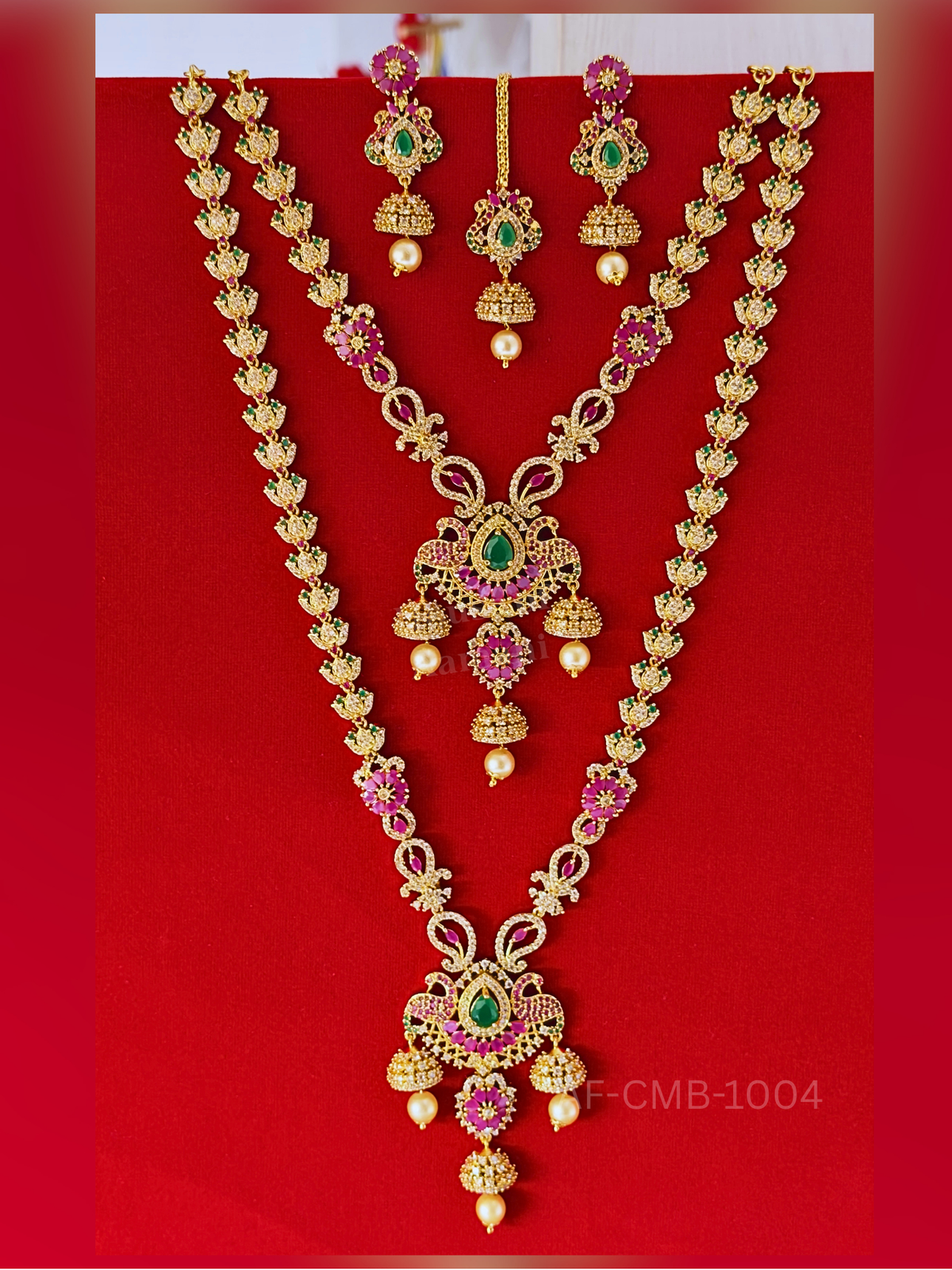 Ruby flowers and sparkling butterfly motifs line the long haram and short necklace, finished with ornate teardrop pendants, pearl accents, earrings, and maang tikka.