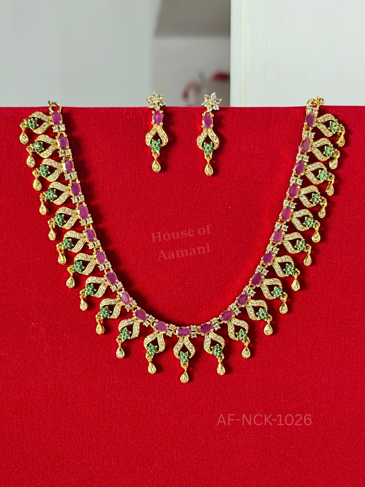 Crystal-studded leaf motifs strung with oval rubies and emerald florets, finished with dainty teardrop danglers and matching earrings.