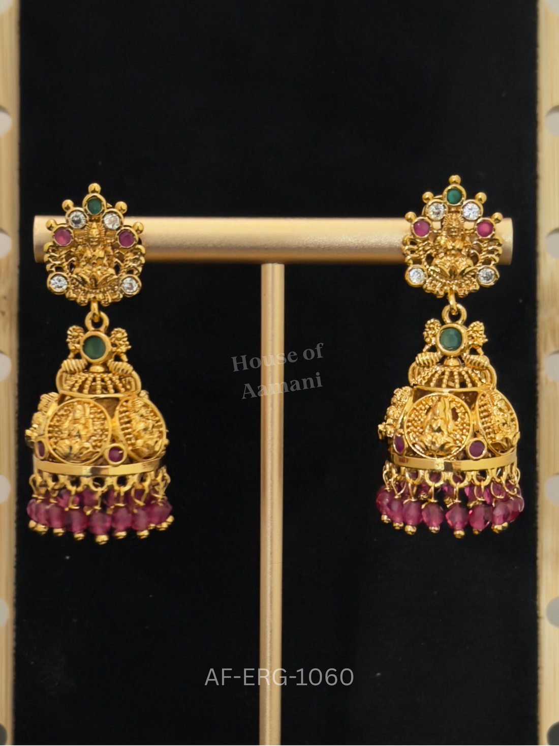 Temple-style jhumkas featuring Goddess Lakshmi motifs on both top and dome, with ruby beads and emerald accents.