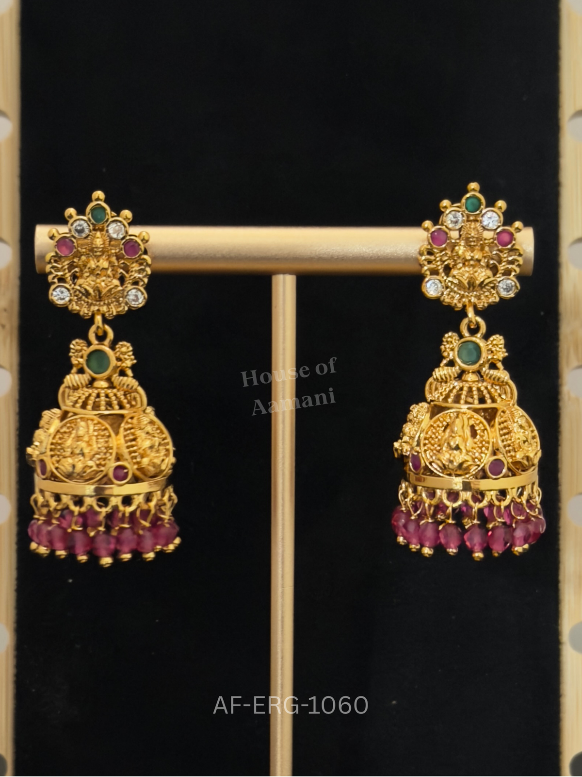 Temple-style jhumkas featuring Goddess Lakshmi motifs on both top and dome, with ruby beads and emerald accents.