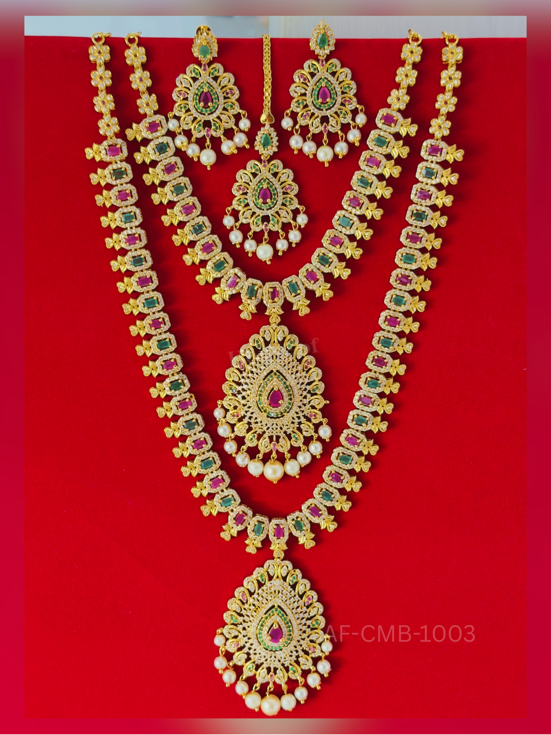 Rectangular ruby and emerald links lead to a large crystal-studded teardrop pendant with pearl drops, paired with a short necklace, earrings, and maang tikka.