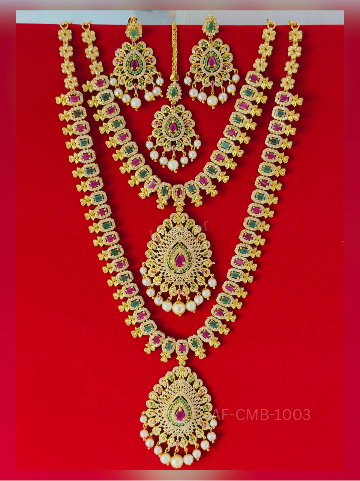 Rectangular ruby and emerald links lead to a large crystal-studded teardrop pendant with pearl drops, paired with a short necklace, earrings, and maang tikka.