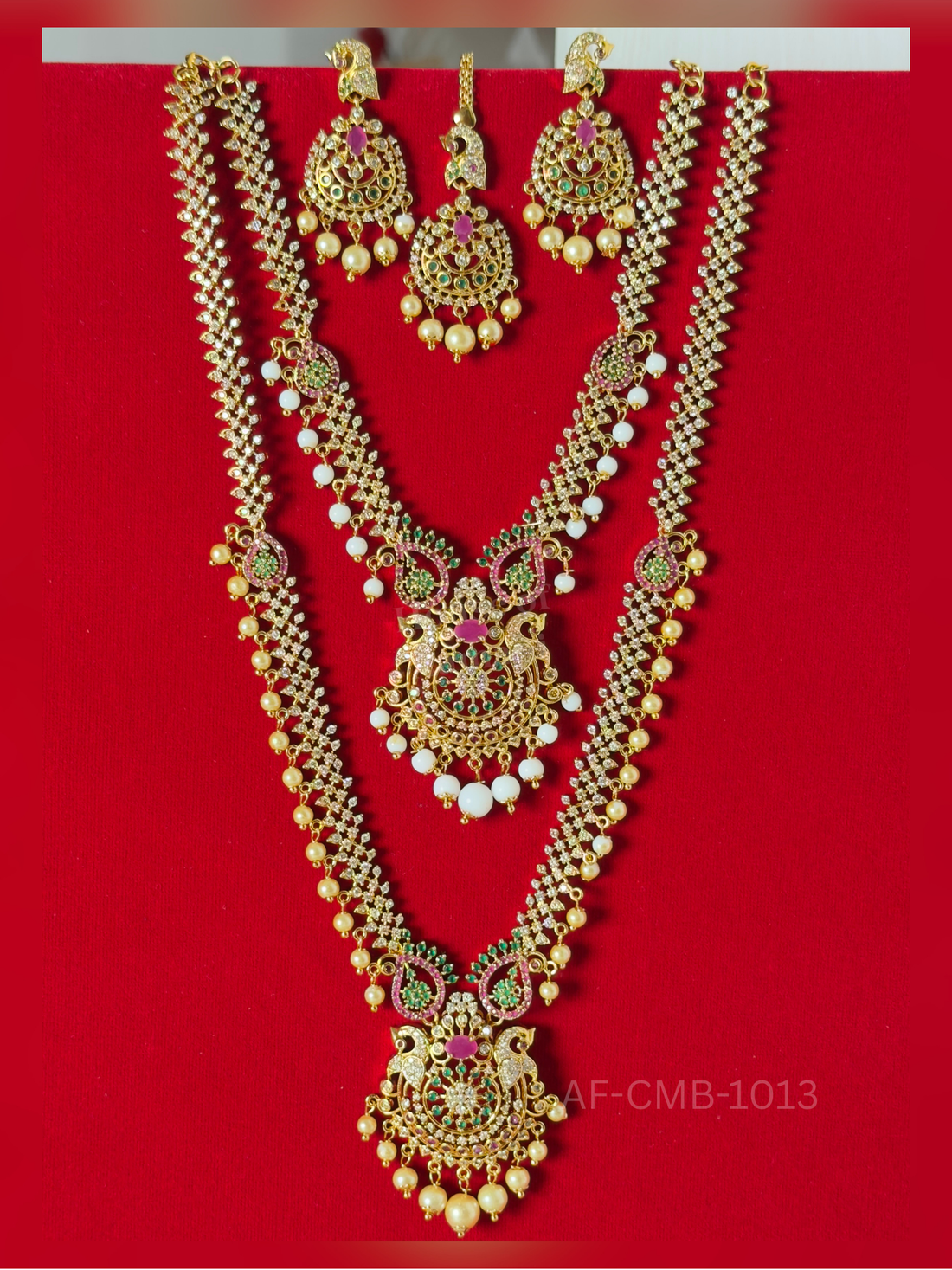 A sparkling crystal chain with pearl and white bead drops meets a peacock pendant in ruby and emerald, with matching earrings and maang tikka.