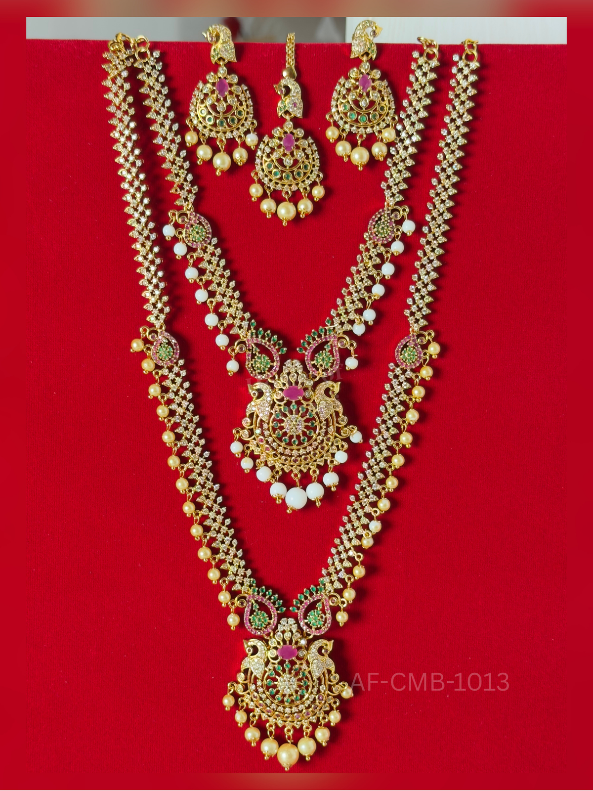 A sparkling crystal chain with pearl and white bead drops meets a peacock pendant in ruby and emerald, with matching earrings and maang tikka.